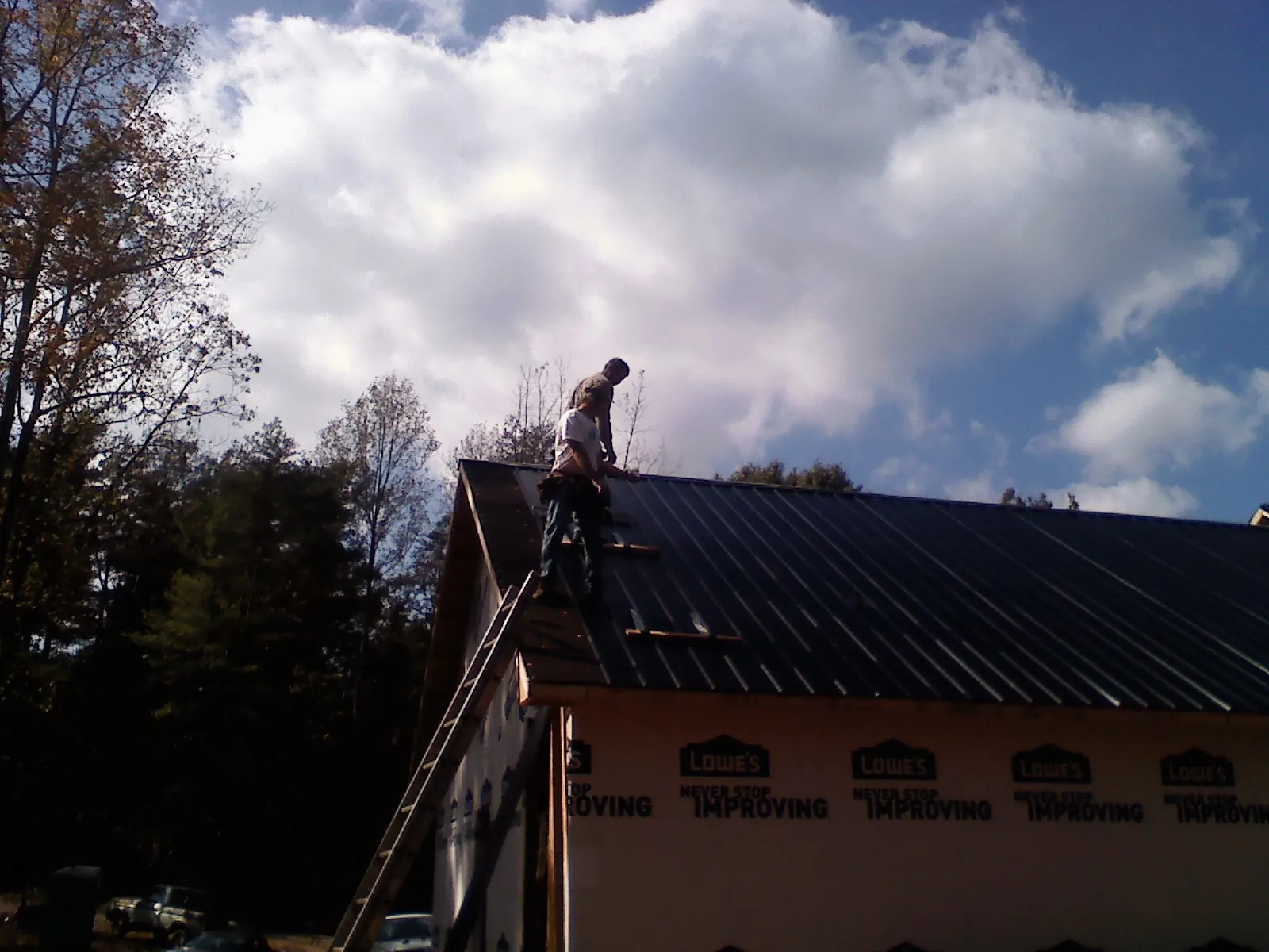 Roofer fastening dark metal panels high against a cloudy sky, from a Roof Inspection job in New Salem